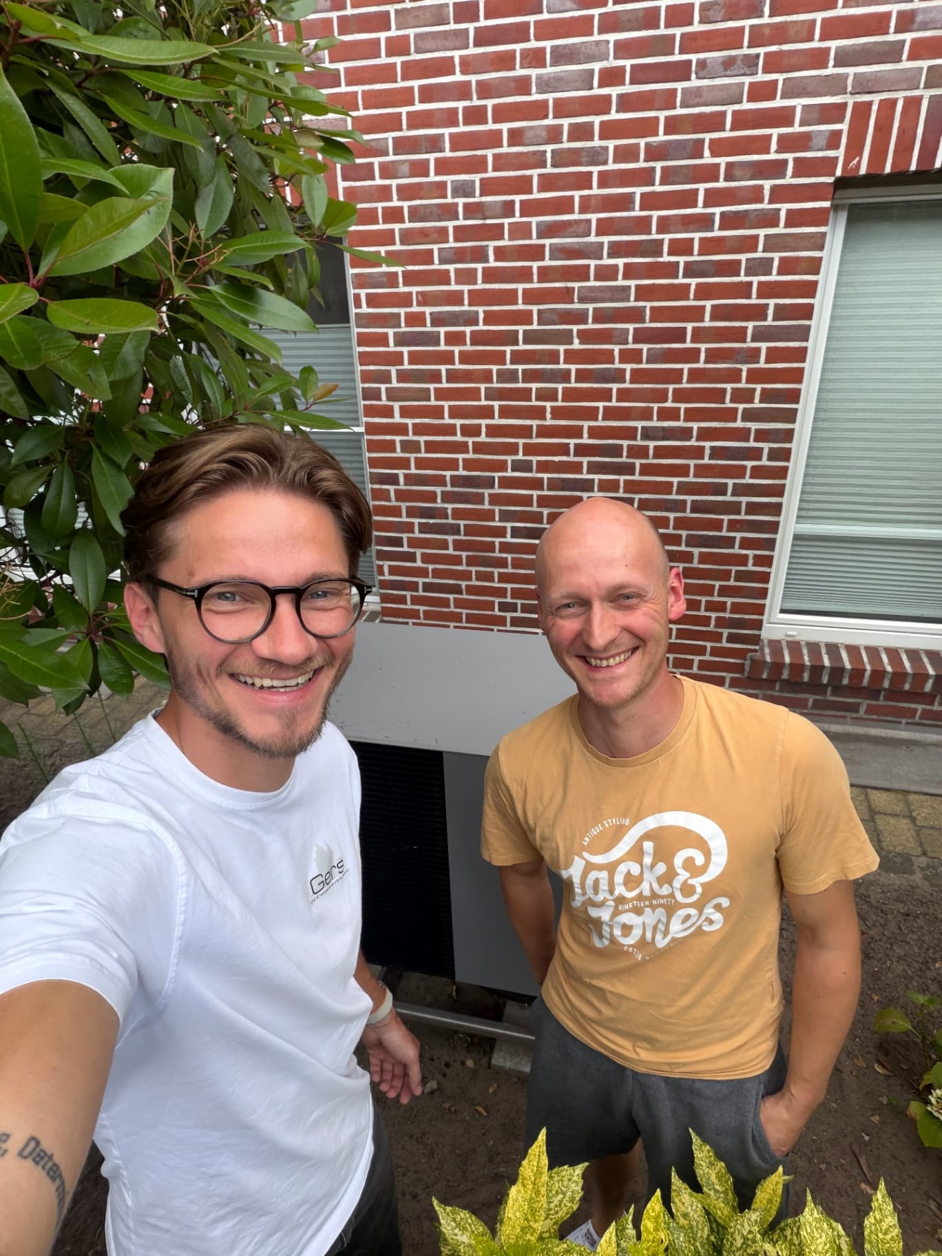 Damian Gers mit einem Kunden vor dessen neuer Waermepumpe an der Hauswand