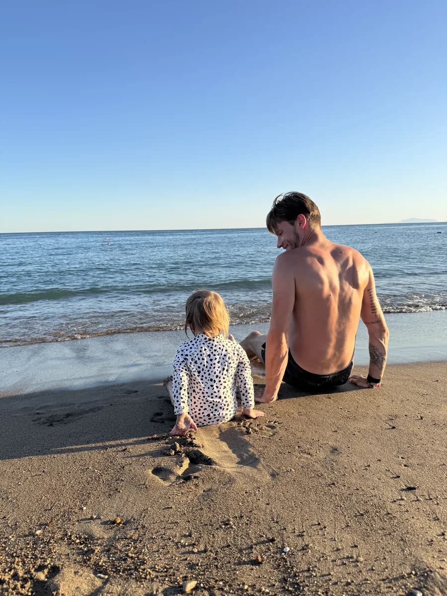 Vater und Kleinkind sitzen am Strand und spielen im Sand